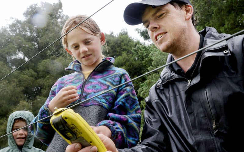 Farm manager Sam Waugh shows Finn Grant from Nina Busing Kindergarten and home-school pupil Sky Ryan how to check the voltage on the electric fence.