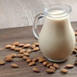 Almond milk in a glass jug on a wooden table. almonds and milk