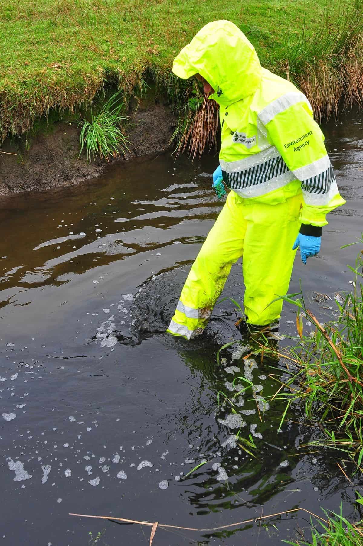 An Environment Agency employee in the River Inny after black sludge entered the watercourse in the summer of 2018 