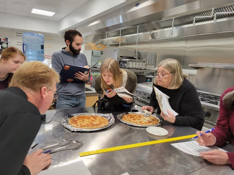 Cheese testers lean in to inspect pizzas at the University of Wisconsin's Center for Dairy Research in Madison. Maayan Silver/WUWM